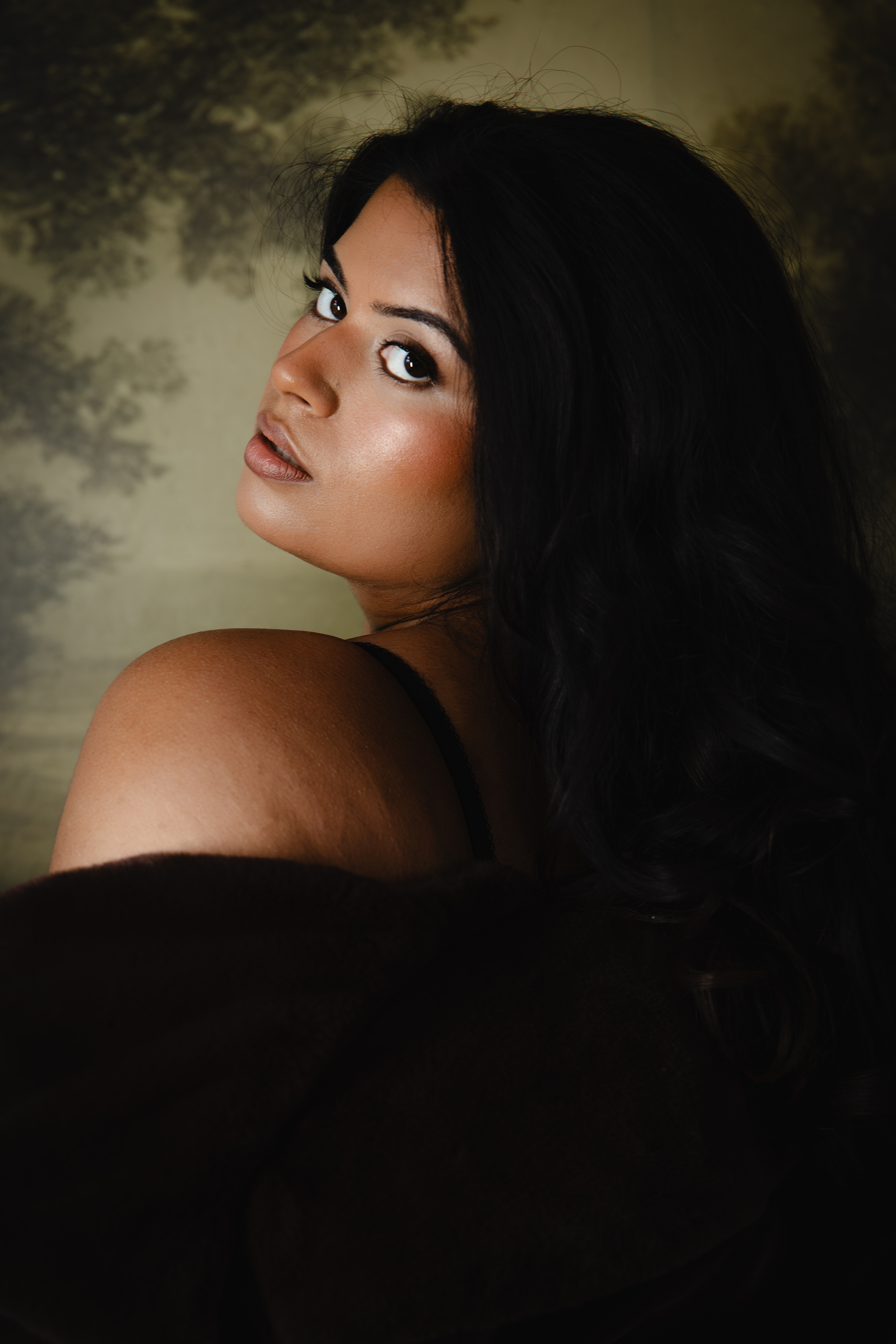 A client looking over her shoulder, wrapped in dark fabric against an olive backdrop