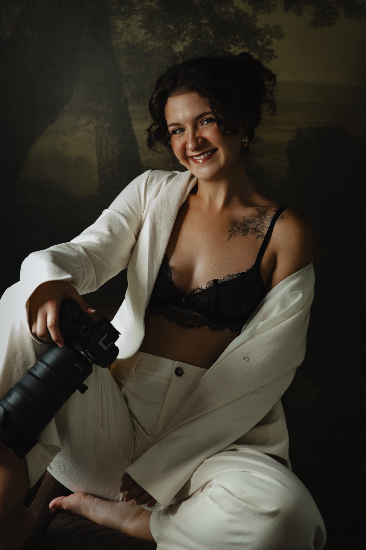 Me smiling in my studio, seated with my camera in a white suit